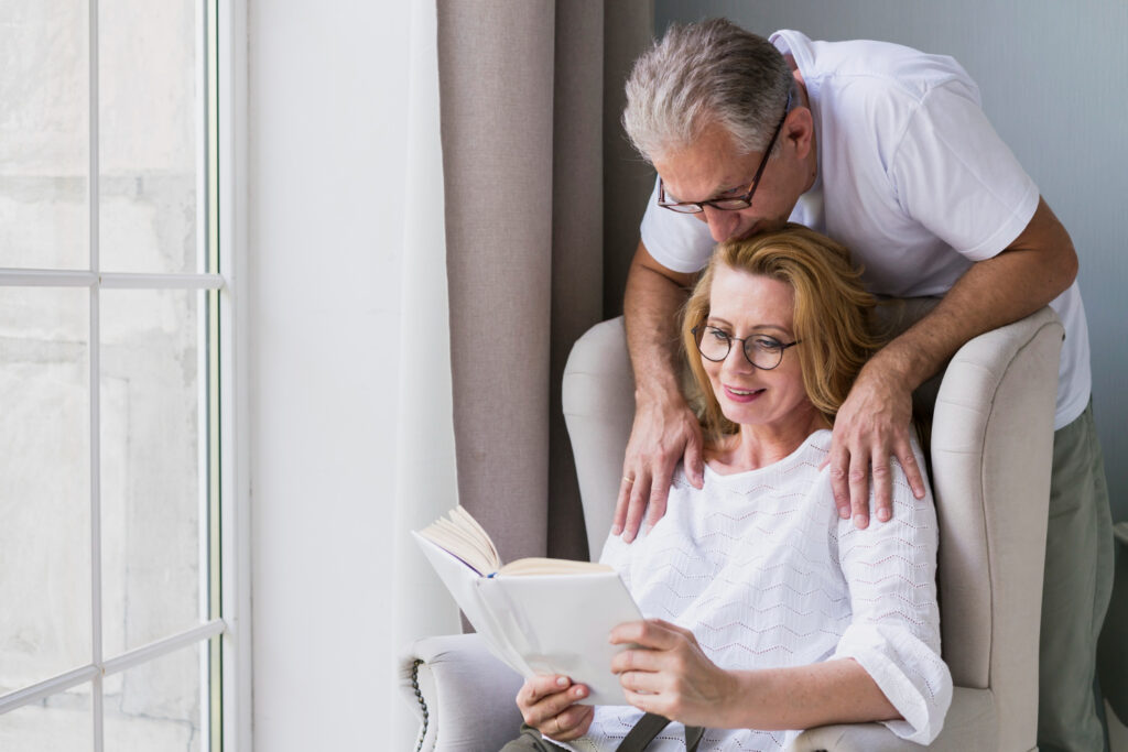 Para w średnim wieku spędza spokojne popołudnie w domu, czytając książkę w okularach do pomieszczeń. Okulary do pomieszczeń zapewniają im wyraźne i komfortowe widzenie w codziennych zajęciach.